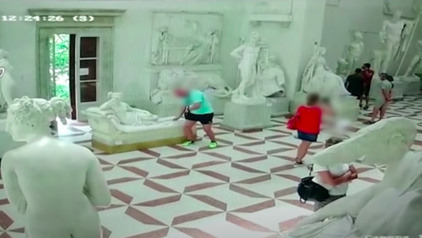 Trong clip có thể thấy rõ một người đàn ông mặc áo phông màu xanh lá cây, màu sáng và quần đùi đen chụp ảnh, rồi ngồi lên tác phẩm của nhà điêu khắc Antonio Canova - Sputnik Việt Nam