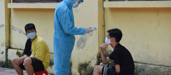 Nhân viên y tế mặc quần áo bảo hộ kiểm tra thân nhiệt của một người ở Hà Nội. - Sputnik Việt Nam