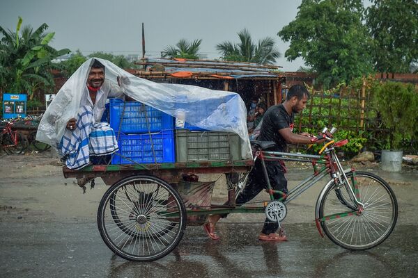 Một người đàn ông ngồi tránh mưa trên xe kéo trong trận mưa bão ở Dhaka - Sputnik Việt Nam