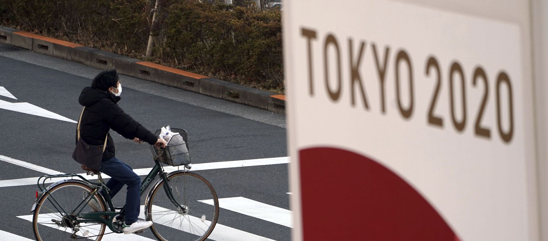 Một người đi xe đạp đeo khẩu trang bảo vệ trên nền biểu ngữ Thế vận hội Tokyo 2020 - Sputnik Việt Nam, 1920, 21.07.2021