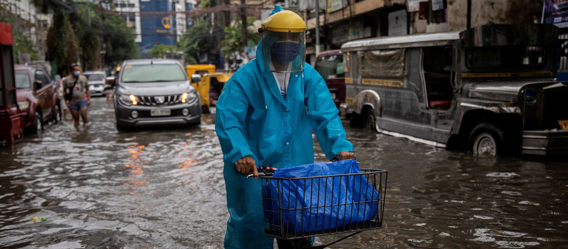 Một người đàn ông đeo mặt nạ đạp xe dọc con phố ngập lụt ở Manila, Philippines. - Sputnik Việt Nam, 1920, 24.07.2021