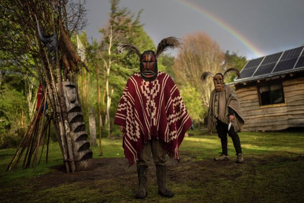 Những người đàn ông Mapuche mang mặt nạ nghi lễ tạo dáng chụp ảnh bên ngoài nhà của họ ở Karimallin, miền nam Chile. - Sputnik Việt Nam