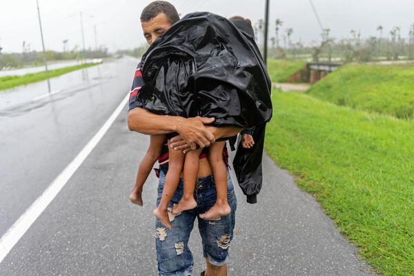 Người đàn ông chở hai đứa trẻ đi trú mưa sau khi cơn bão Yang làm ngập nhà của họ ở Pinar del Rio, Cuba. - Sputnik Việt Nam