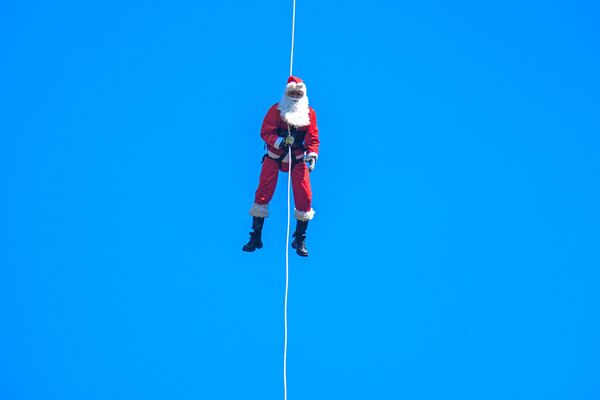 Lính cứu hỏa thành phố Hector Chacon, hóa trang thành ông già Noel, đu dây từ một cây cầu để phát quà cho trẻ em ở Guatemala. - Sputnik Việt Nam