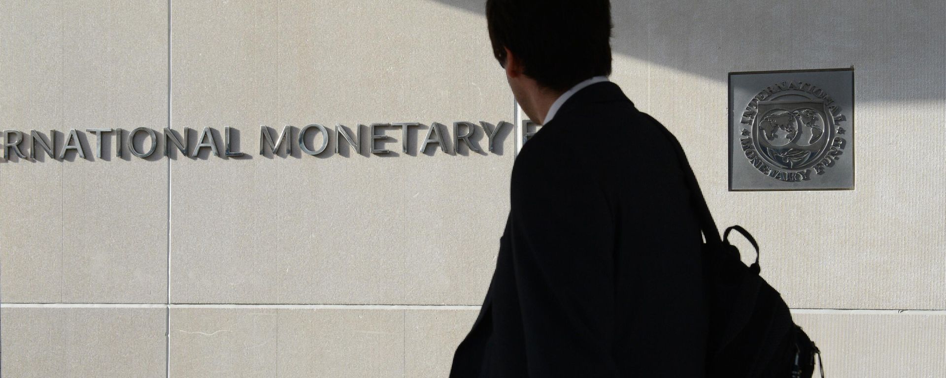 Một người đàn ông bên ngoài Quỹ Tiền tệ Quốc tế nhìn vào logo của IMF trên tường - Sputnik Việt Nam, 1920, 09.07.2026
