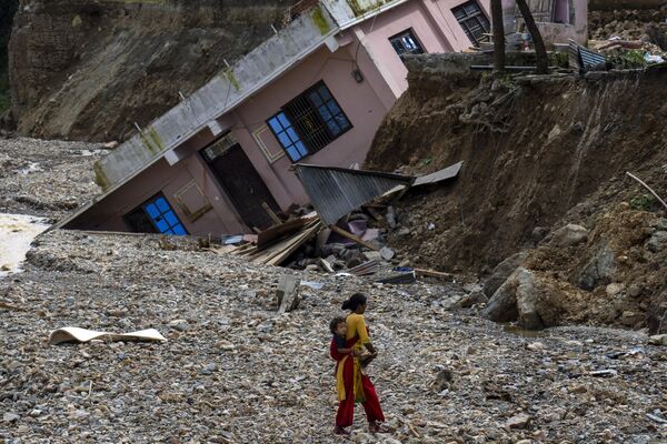 Người phụ nữ và con đi ngang qua ngôi nhà bị lũ cuốn trôi trên sông Nakhu sau trận mưa lớn ở Lalitpur, Nepal - Sputnik Việt Nam