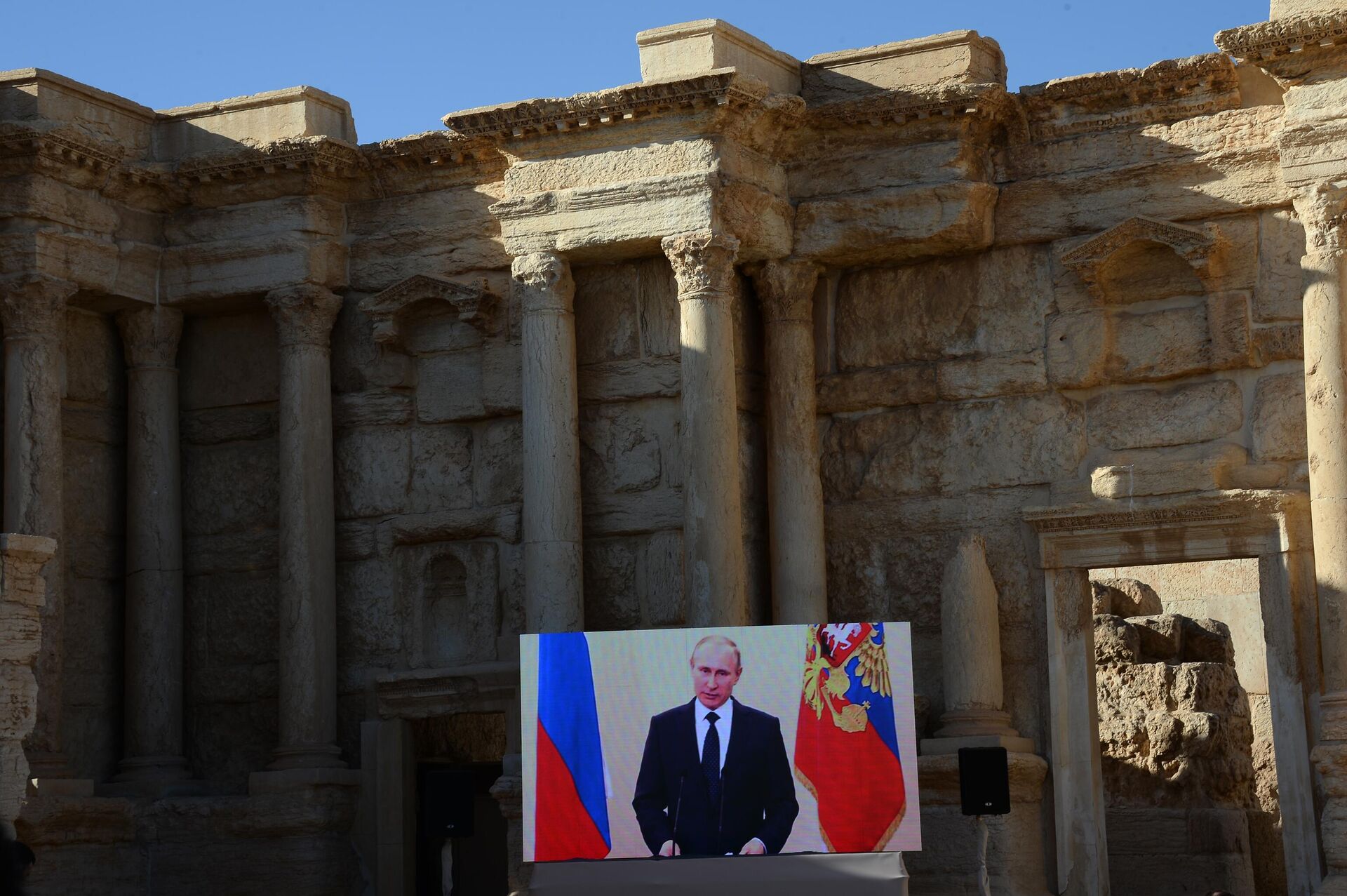 Phát sóng bài phát biểu của Tổng thống Nga Vladimir Ông Putin tại đấu trường La Mã ở Palmyra, Syria, nơi được giải phóng khỏi lực lượng khủng bố Nhà nước Hồi giáo. - Sputnik Việt Nam, 1920, 07.05.2025