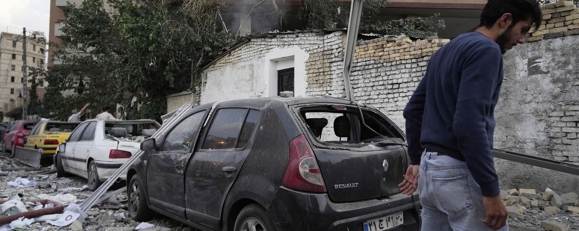 Một người đàn ông đi bộ tại hiện trường vụ nổ ở khu dân cư phía bắc Tehran, Iran, thứ sáu, ngày 13 tháng 6 năm 2025. - Sputnik Việt Nam, 1920, 26.06.2025