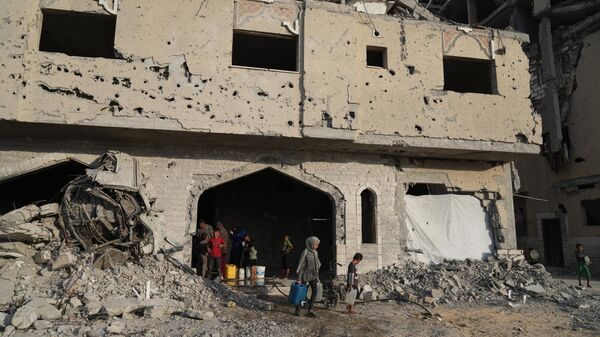 Người dân Palestine di tản lấy nước từ một tòa nhà bị phá hủy ở Khan Younis, Dải Gaza, Thứ Bảy, ngày 18 tháng 10 năm 2025. - Sputnik Việt Nam