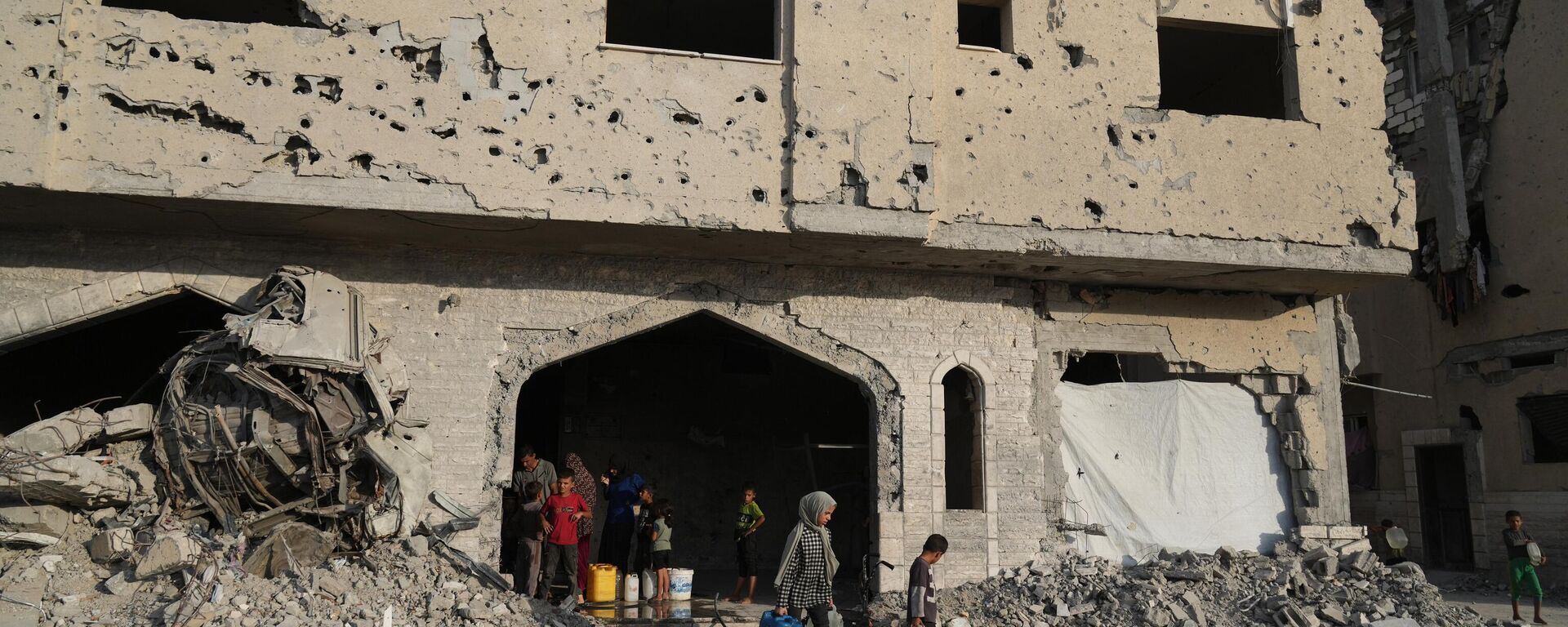 Người dân Palestine di tản lấy nước từ một tòa nhà bị phá hủy ở Khan Younis, Dải Gaza, Thứ Bảy, ngày 18 tháng 10 năm 2025. - Sputnik Việt Nam, 1920, 20.10.2025