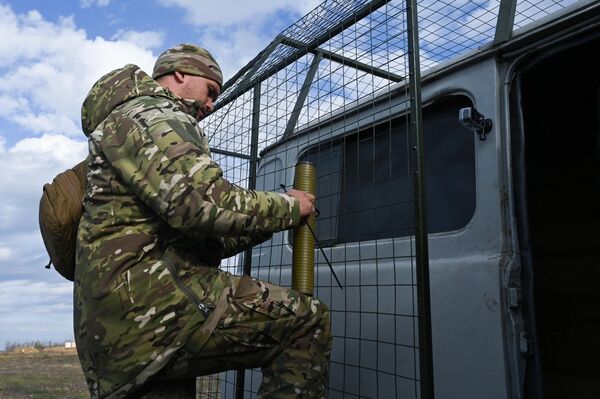 Binh sĩ đang chuẩn bị một chiếc xe được lắp đặt hệ thống lưới sắt bảo vệ (kiểu vỉ nướng) chống tấn công UAV cho đợt thử nghiệm trên thao trường ở tỉnh Rostov - Sputnik Việt Nam