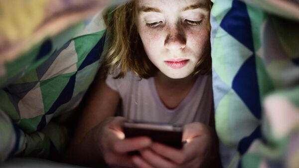 Một cô gái nhìn vào điện thoại di động dưới tấm chăn. - Sputnik Việt Nam