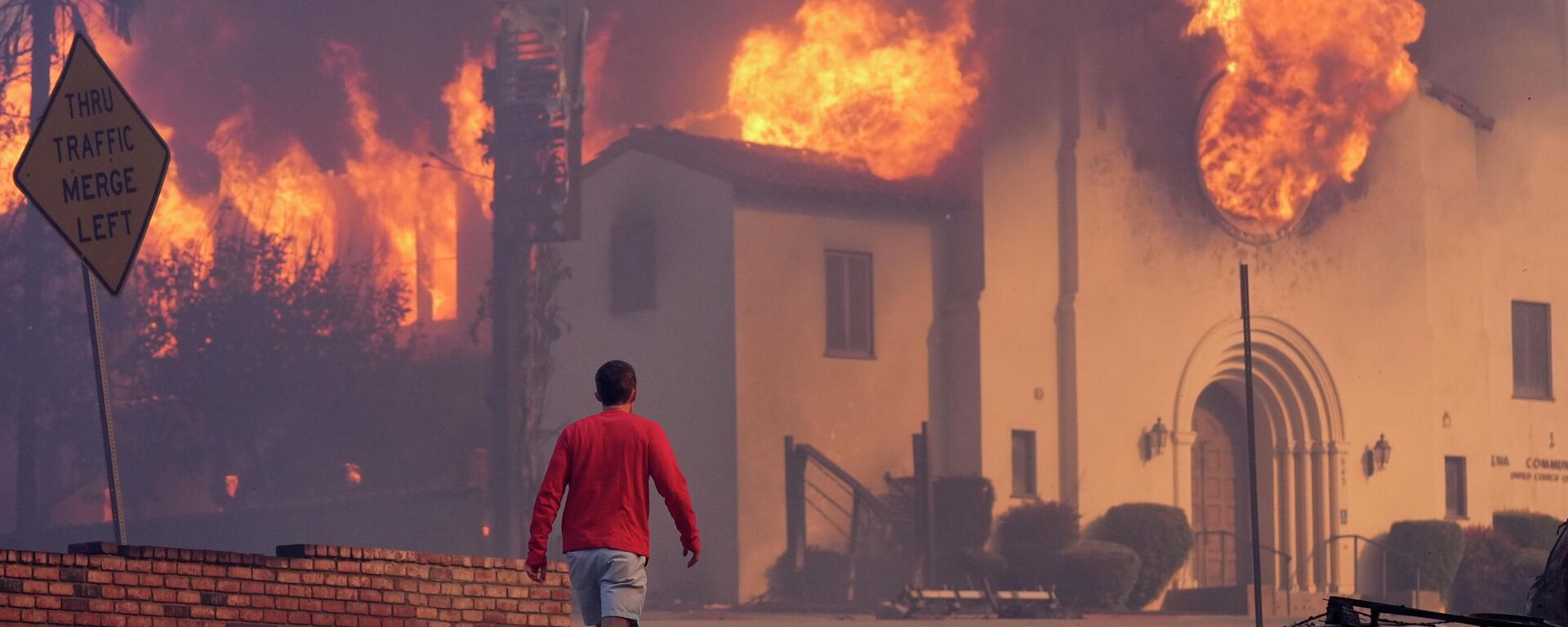 Người đàn ông đi ngang qua nhà thờ Altadena Community đang bốc cháy dữ dội do các đám cháy rừng ở trung tâm thành phố Altadena, Pasadena, California, Mỹ - Sputnik Việt Nam, 1920, 21.12.2025