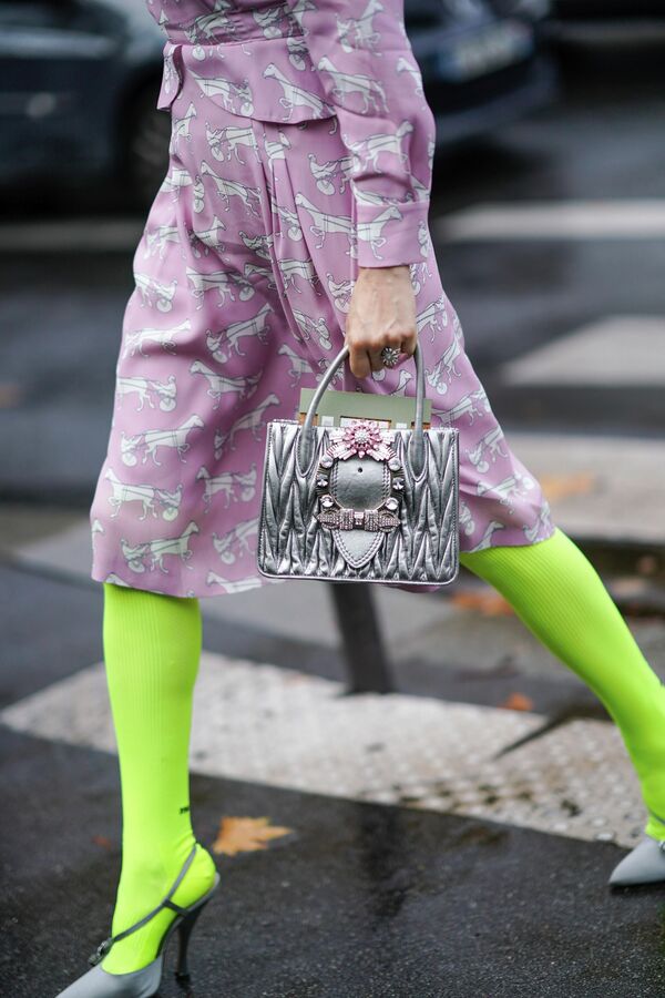 Vị khách đeo túi xách Miu Miu màu bạc và mặc váy màu hồng nhạt có họa tiết người đua ngựa và ngựa trắng trước cửa hàng Miu Miu trong Tuần lễ thời trang Paris, Pháp, 2019 - Sputnik Việt Nam