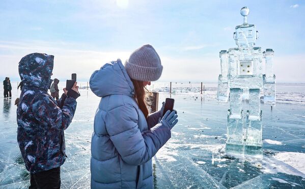 Những người tham gia Lễ hội nghệ thuật băng giá mùa đông lần thứ XII "Sống trên Baikal" 2026 bên tác phẩm điêu khắc hình robot - Sputnik Việt Nam