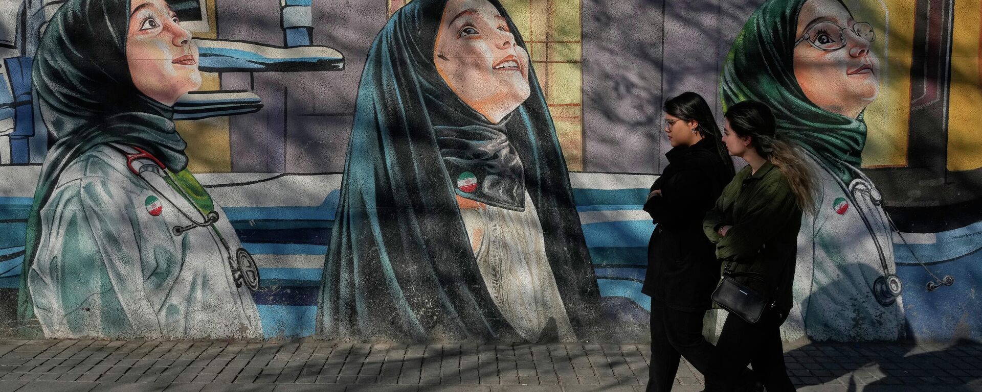 Phụ nữ đi ngang qua một bức bích họa tại trường nữ sinh trên phố Enghelab-e-Eslami ở Tehran, Iran. - Sputnik Việt Nam, 1920, 03.03.2026