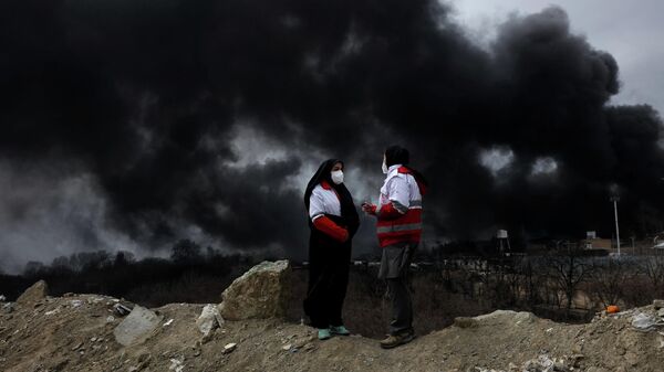 Các thành viên Hội Chữ thập đỏ nói chuyện với nhau khi khói bốc lên sau một vụ tấn công được báo cáo vào các bể chứa nhiên liệu ở Shahran, Iran - Sputnik Việt Nam