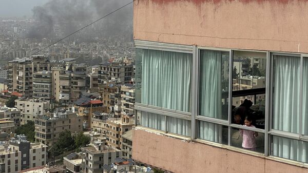 Một cô gái nhìn ra ngoài cửa sổ khi khói bốc lên sau cuộc không kích của Israel vào vùng ngoại ô phía nam Beirut, Lebanon - Sputnik Việt Nam