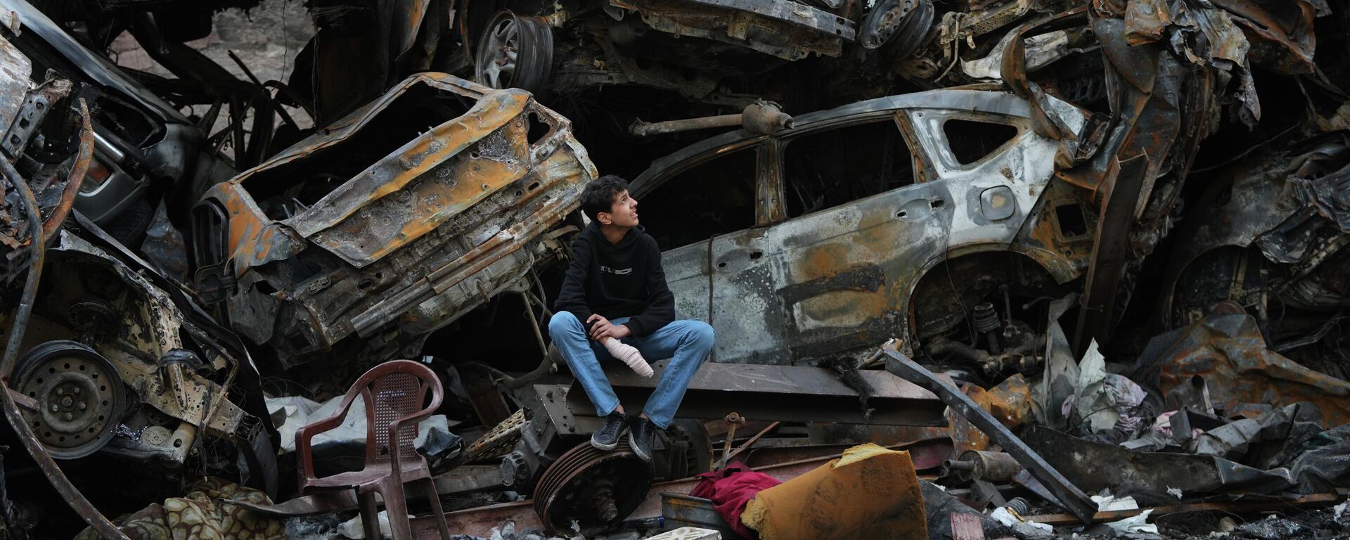 Một người đàn ông ngồi cạnh những chiếc xe bị cháy rụi và đống đổ nát của một tòa nhà ở Beirut, Lebanon. - Sputnik Việt Nam, 1920, 20.04.2026