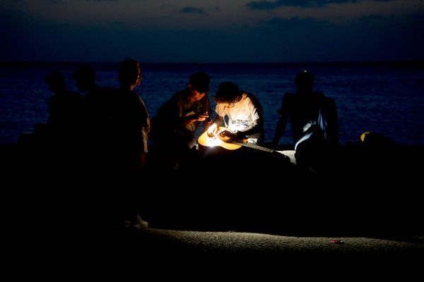 Một người đàn ông sửa dây đàn guitar bằng đèn pin trên đại lộ Malecon trong lúc mất điện ở Havana. - Sputnik Việt Nam