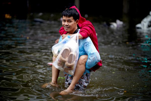Người đàn ông xách đồ mua sắm trên con phố ngập nước ở Bangkok. - Sputnik Việt Nam