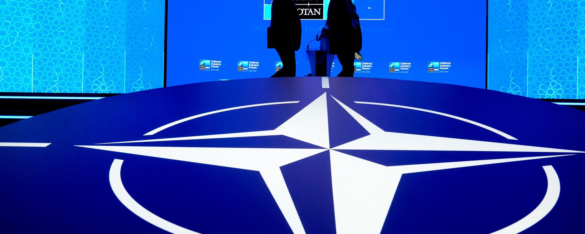 Hai người đàn ông đi ngang qua biểu tượng của NATO - Sputnik Việt Nam, 1920, 14.10.2026