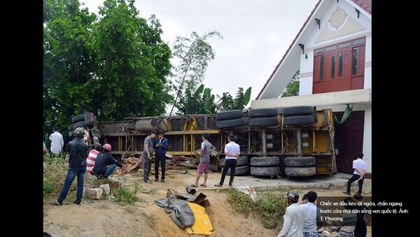 Chiếc xe đầu kéo lật ngửa, chắn ngang trước cửa nhà dân sống ven quốc lộ. - Sputnik Việt Nam