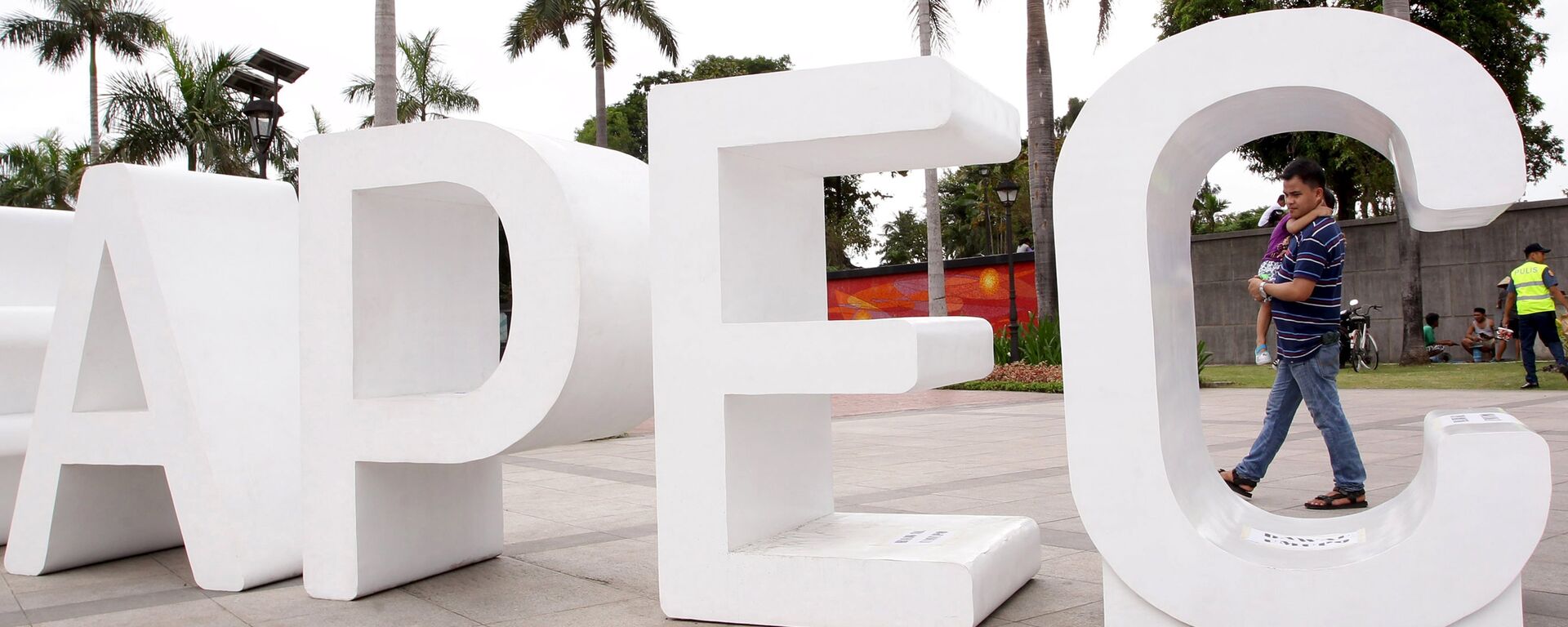 A resident carries his child past an Asia-Pacific Economic Cooperation (APEC) sign in Manila's Rizal park, where the APEC summit will be held next week, in Manila November 15, 2015 - Sputnik Việt Nam, 1920, 11.07.2025