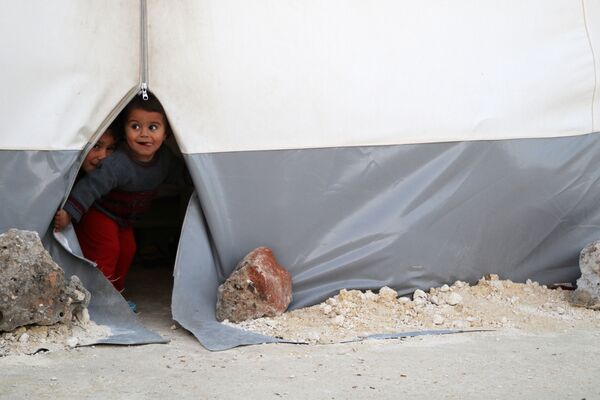 Những đứa trẻ ngó ra từ trại lều bạt tạm thời dành cho dân sơ tán từ Đông Ghouta ở tỉnh Idlib của Syria - Sputnik Việt Nam