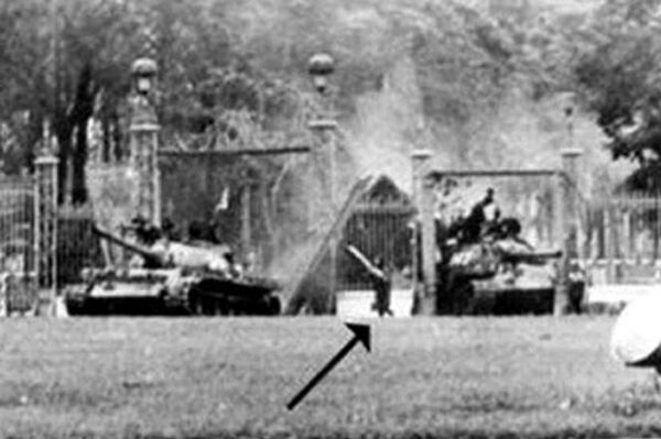 Tấm ảnh của nữ nhà báo Pháp Francoise Demulder chụp lại khoảnh khắc lịch sử ngày 30/4/1975: Xe tăng 390 húc văng hai cánh cửa cổng chính, còn xe tăng 843 bị kẹt ở cổng phụ bên trái Dinh Độc Lập. Đại đội trưởng Bùi Quang Thận xuống xe, cầm cờ chạy bộ vào Dinh Độc Lập (mũi tên). - Sputnik Việt Nam