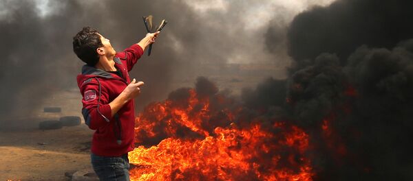 A Palestinian man uses a slingshot during clashes with Israeli forces along the border with the Gaza strip east of Khan Yunis on May 14, 2018, as Palestinians protest over the inauguration of the US embassy following its controversial move to Jerusalem - Sputnik Việt Nam