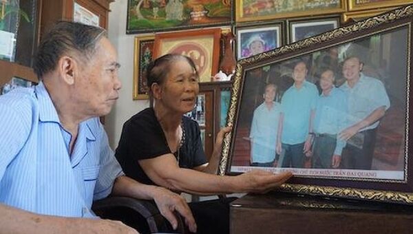 Vợ chồng thầy Lê Kim Toàn ngắm bức ảnh chụp cùng Chủ tịch nước Trần Đại Quang trong dịp học trò cũ về thăm quê năm 2016. - Sputnik Việt Nam