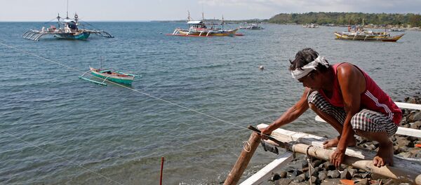 Một ngư dân đang sửa thuyền của mình, trông ra xa là  chiếc thuyền đánh cá đang hoạt động ở bãi biển tranh chấp ở Biển Đông, tại Masinloc, Zambales, Philippines - Sputnik Việt Nam