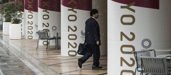Một người đàn ông trên nền các biểu ngữ với các biểu tượng của Thế vận hội 2020 tại Tokyo - Sputnik Việt Nam