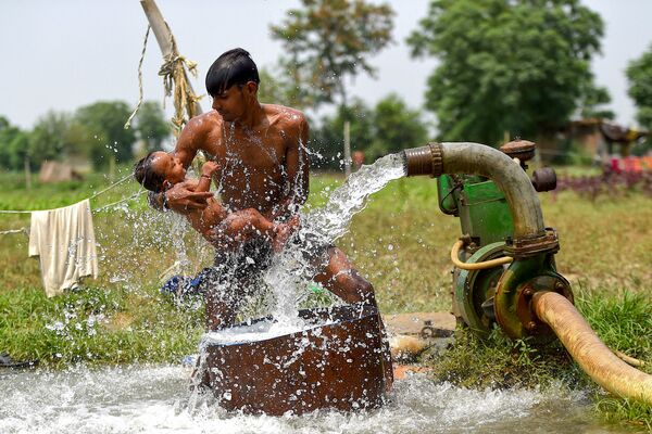 Người đàn ông với đứa bé ngâm mình dưới giếng trong lúc nắng nóng ở New Delhi, Ấn Độ - Sputnik Việt Nam